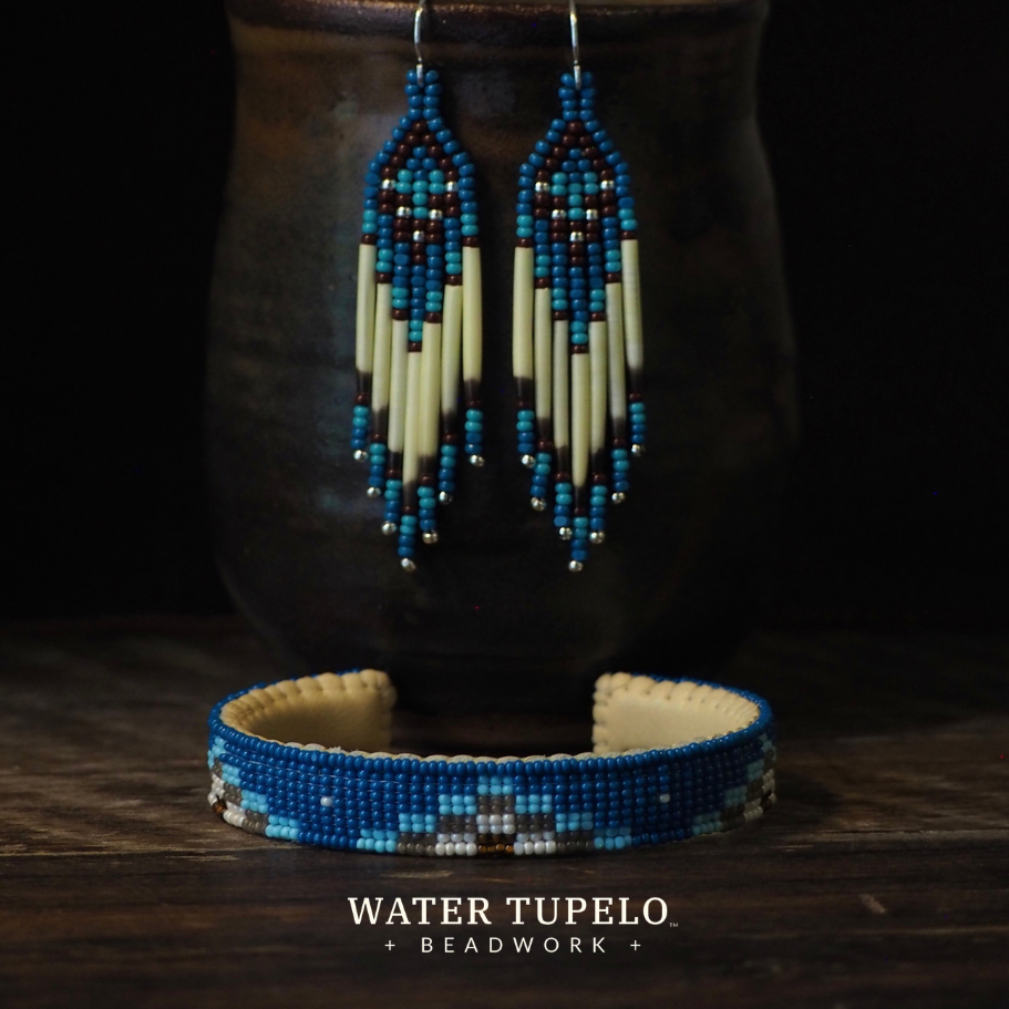 Blue and cream beaded hoop earrings and a matching beaded bracelet displayed on a dark ceramic cup against a black background, with the brand name Water Tupelo Beadwork at the bottom.